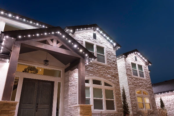 Downlit permanent lighting washing the stone facade of a craftsman-style home