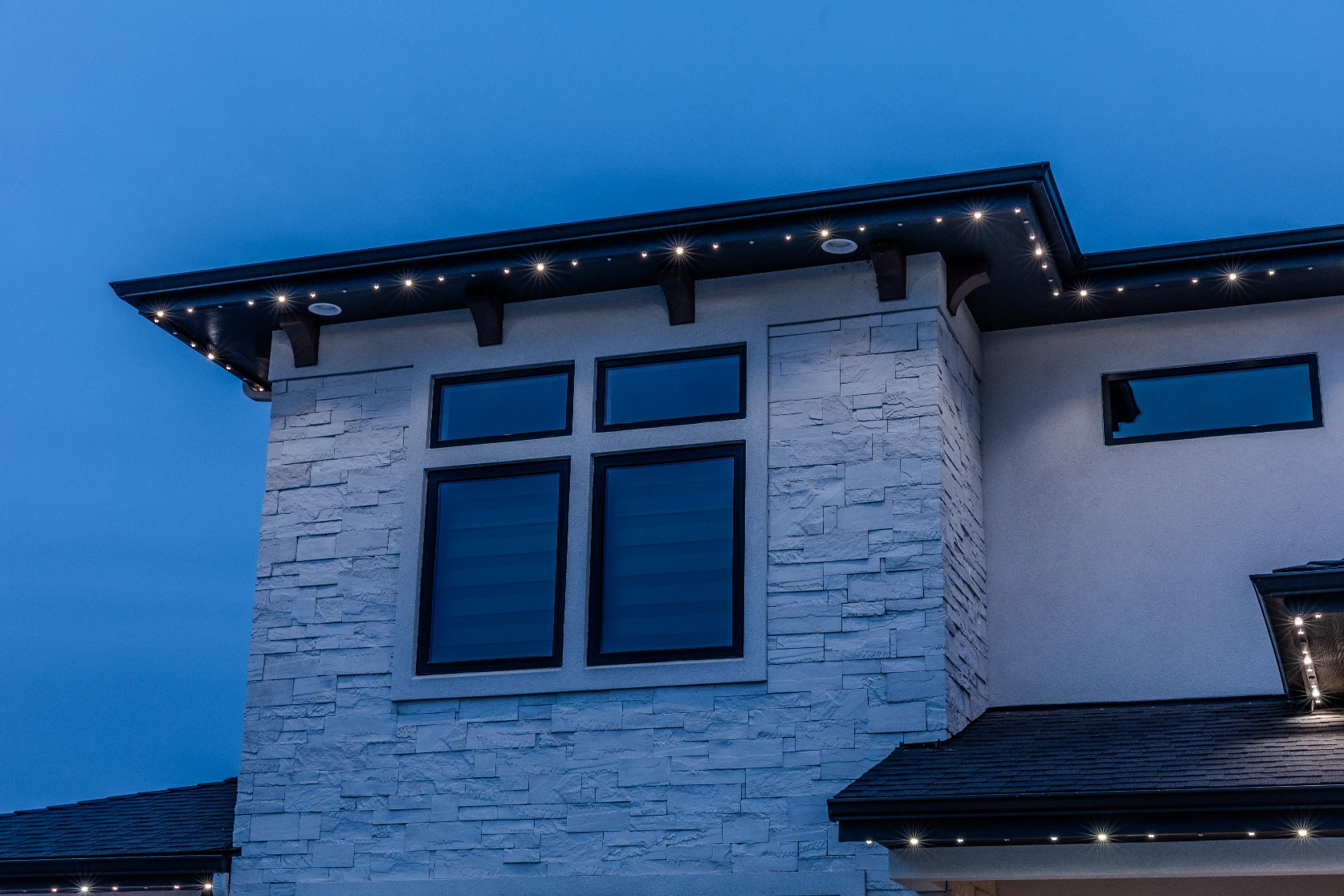 Aerial view of a home with warm white roofline lighting glowing at night