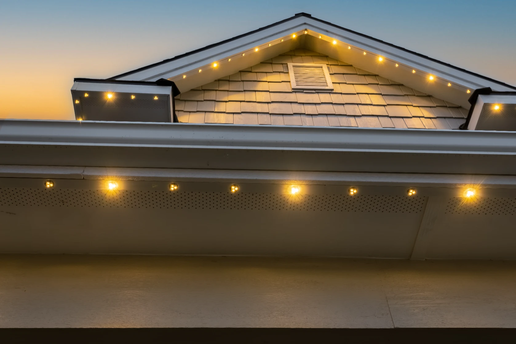 Warm white eave lights reflecting off a wet driveway after rain