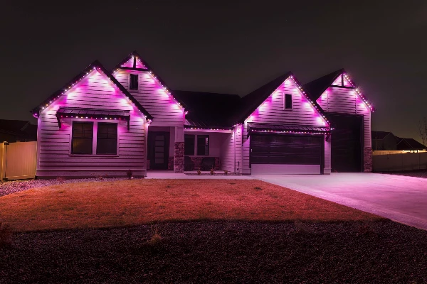 Red and green Christmas lighting alternating along the roofline of a two-story home